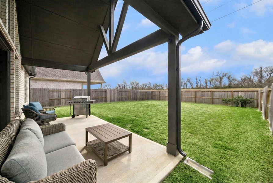 THE COVERED BACK PATIO INCLUDES A CONCRETE FLOOR AND A VIEW OF THE FULLY FENCED, GRASS-COVERED BACKYARD.