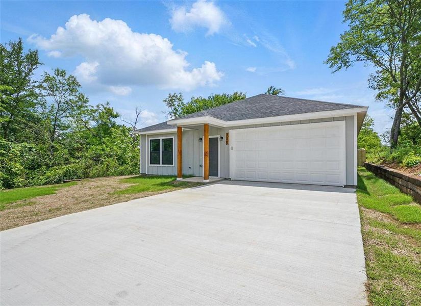 View of front facade featuring board and batten siding, driveway, a front lawn, an attached garage, and a shingled roof
