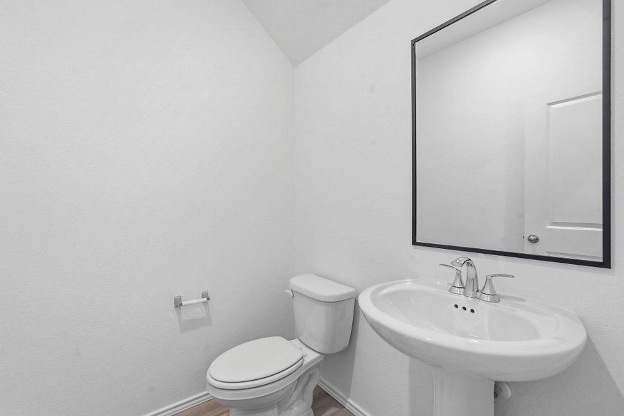 Pedestal sink with chrome fixtures, a modern frameless mirror, and wood-finish flooring Pedestal sink with chrome fixtures, a modern frameless mirror, and wood-finish flooring