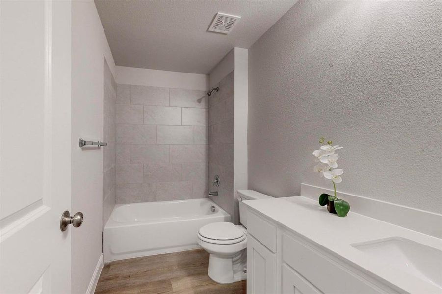 Full bathroom featuring vanity, toilet, tiled shower / bath combo, a textured ceiling, and hardwood / wood-style floors