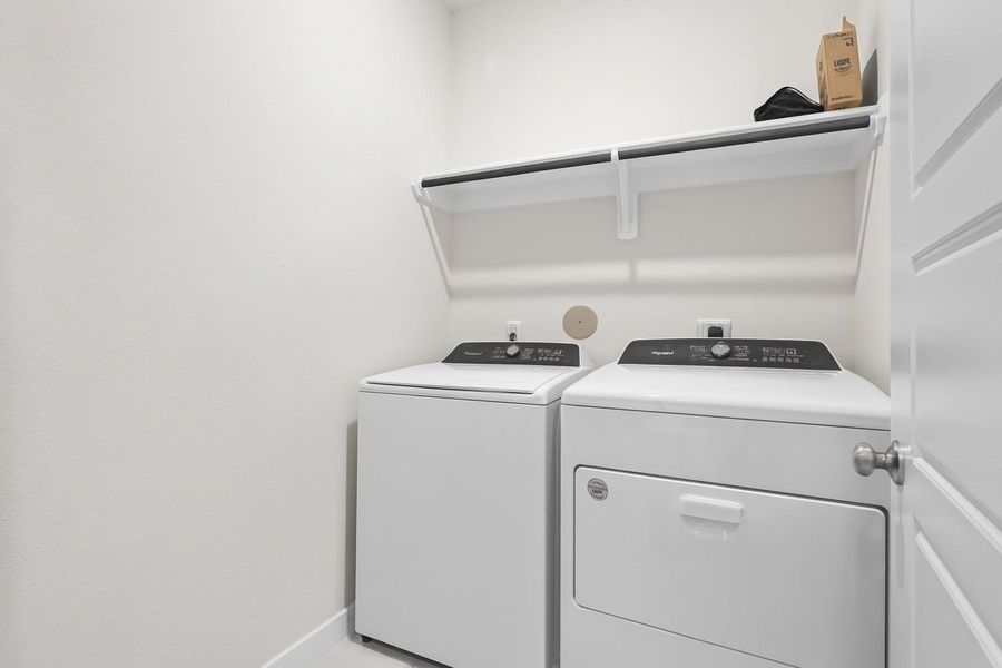 This photo shows a compact laundry room with a washer and dryer, a shelf above for storage, and a clean, neutral color scheme.