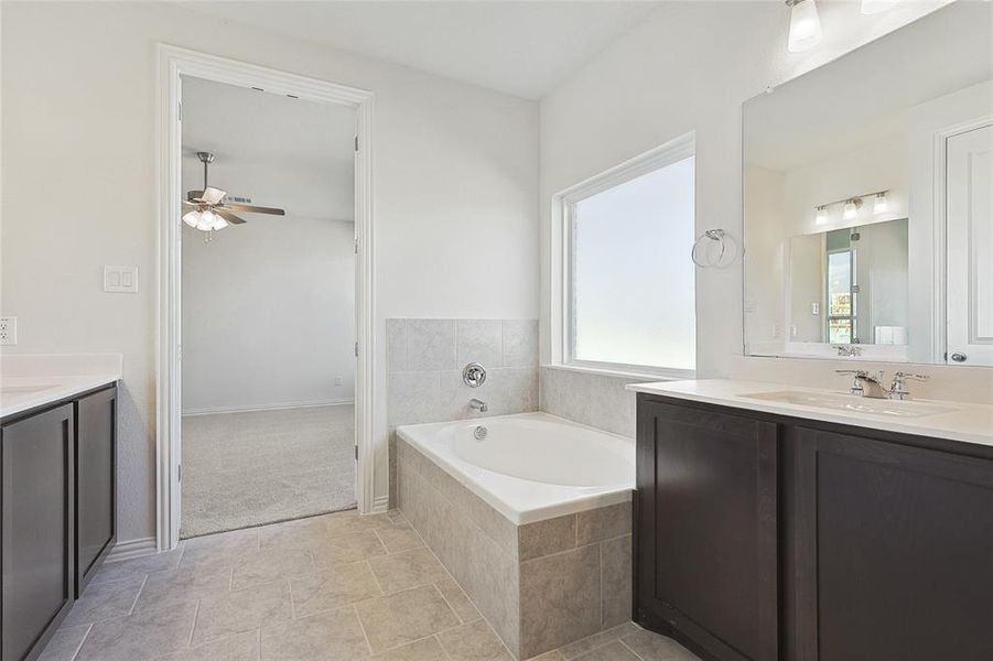 Bathroom with tile flooring, tiled bath, ceiling fan, and vanity