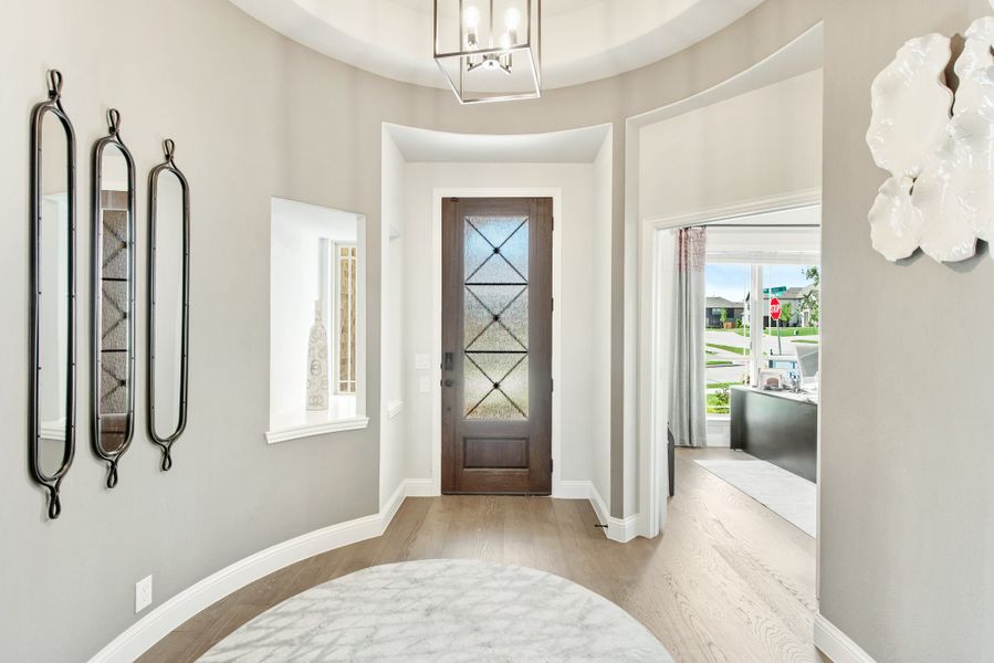 Rounded foyer with wood front door, glass panels, chandelier, and light hardwood floors Rounded foyer with wood front door, glass panels, chandelier, and light hardwood floors