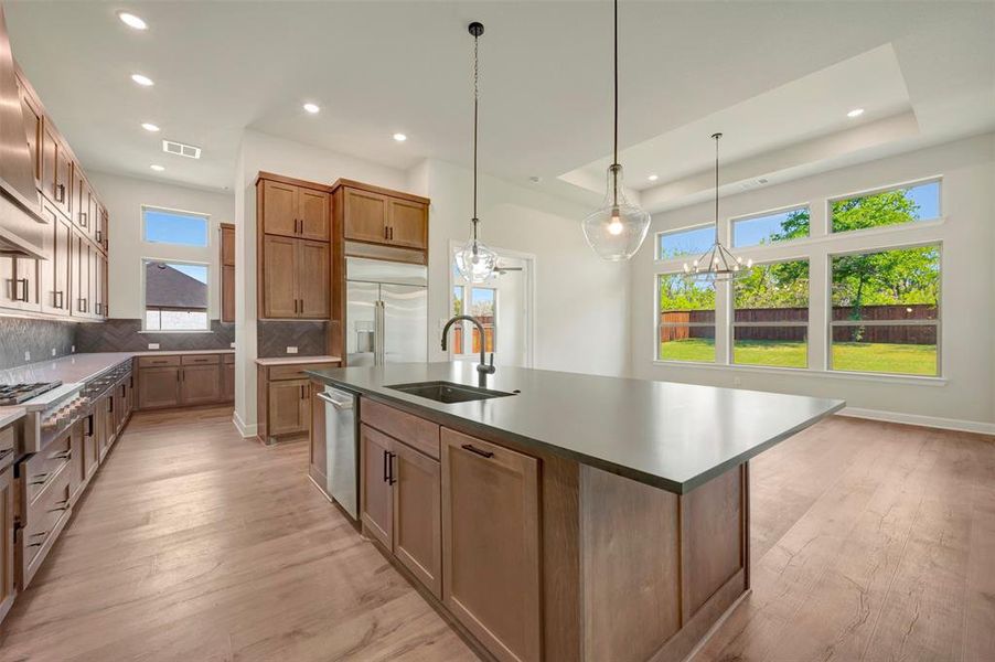 Kitchen featuring wood finish cabinets, light wood-type flooring, a kitchen island with sink, decorative backsplash, and a tray ceiling