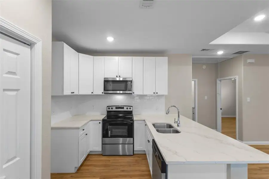 Kitchen with a peninsula, appliances with stainless steel finishes, white cabinets, light stone counters, and recessed lighting