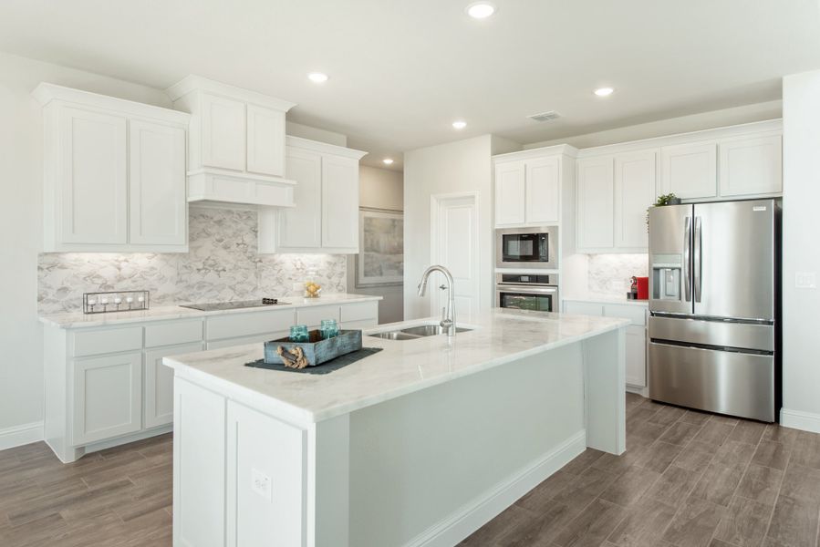 Kitchen with white cabinets, center island with sink, stainless steel appliances, and wood-look tile floors