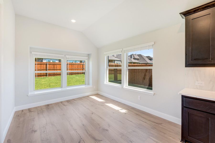 Bright empty room with vaulted ceiling, light wood floors, and large windows overlooking a fenced backyard Bright empty room with vaulted ceiling, light wood floors, and large windows overlooking a fenced backyard