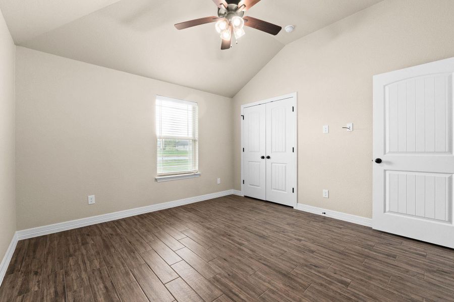 Spare room featuring dark wood like tile floors, lofted ceiling, and a ceiling fan, and a closet Spare room featuring dark wood like tile floors, lofted ceiling, and a ceiling fan, and a closet
