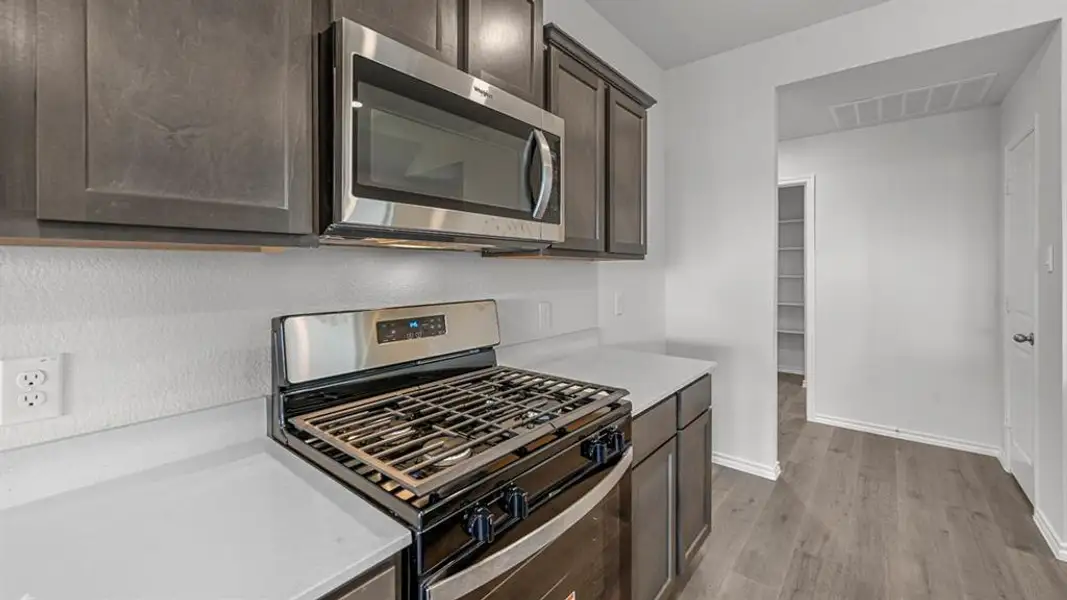 Kitchen featuring dark wood-finish cabinetry, stainless steel microwave, gas range with oven, light-toned countertops, and wood-finish flooring