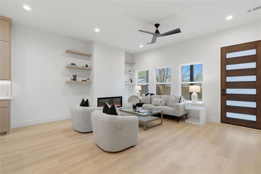 Living area with light wood finished floors, a ceiling fan, a glass covered fireplace, recessed lighting, and built in features Living area with light wood finished floors, a ceiling fan, a glass covered fireplace, recessed lighting, and built in features