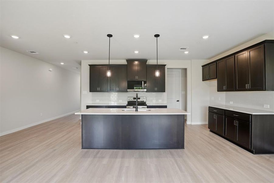 Kitchen featuring tasteful backsplash, hanging light fixtures, recessed lighting, a kitchen island with sink, and light wood finished floors Kitchen featuring tasteful backsplash, hanging light fixtures, recessed lighting, a kitchen island with sink, and light wood finished floors