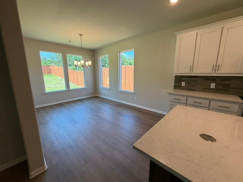 Open-concept living space with wood-finish flooring, a contemporary chandelier, and multiple windows overlooking a private backyard with a wooden fence