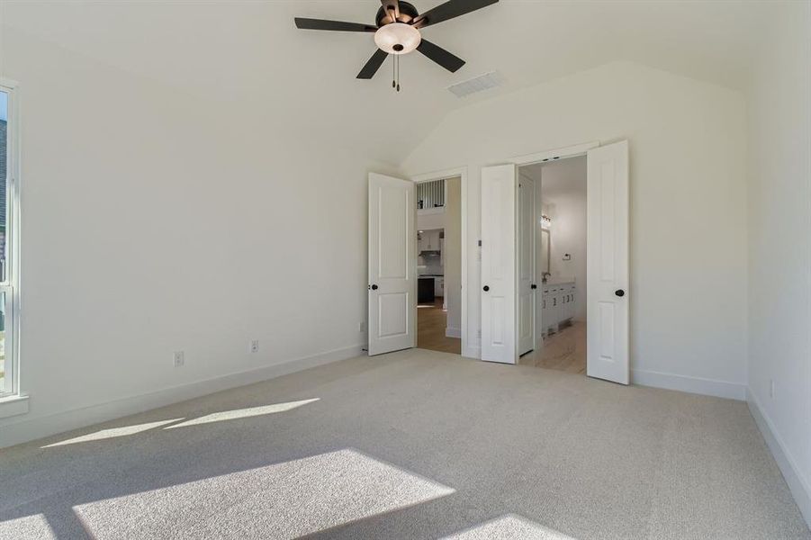 Unfurnished bedroom featuring carpet, connected bathroom, a ceiling fan, and vaulted ceiling