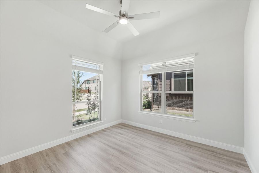 Empty room with vaulted ceiling, ceiling fan, light wood floors, and two windows with neighborhood views Empty room with vaulted ceiling, ceiling fan, light wood floors, and two windows with neighborhood views