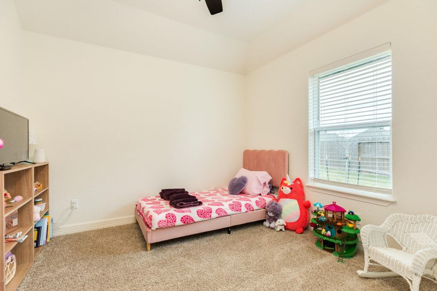 This cozy bedroom features a carpeted floor, a large window for natural light, and ample space for toys and storage.
