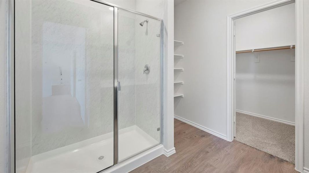 Full bathroom with light wood-style flooring, a walk in closet, and a stall shower