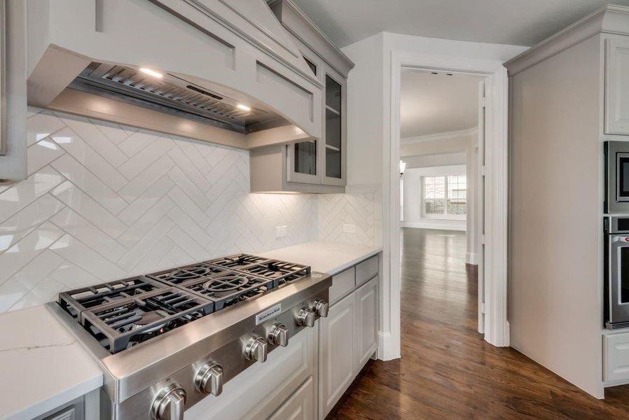 Kitchen featuring dark wood finished floors, glass insert cabinets, custom exhaust hood, appliances with stainless steel finishes, and backsplash