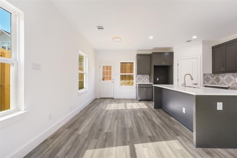 Kitchen featuring tasteful backsplash, light wood-style flooring, recessed lighting, light stone countertops, and a center island with sink