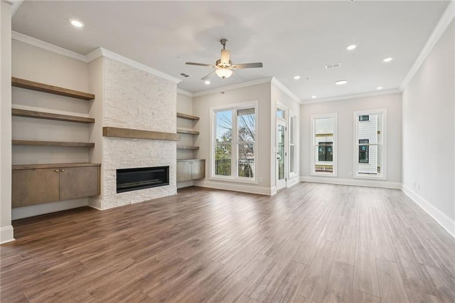 Unfurnished living room featuring a ceiling fan, a stone fireplace, wood finished floors, crown molding, and recessed lighting