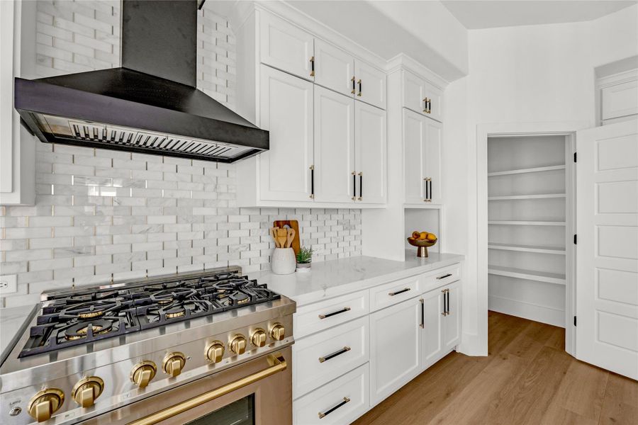Marble subway backsplash with gold inlay, two-toned knurled cabinet hardware, and a walk-in pantry (partially shown here) add style and function to the kitchen.