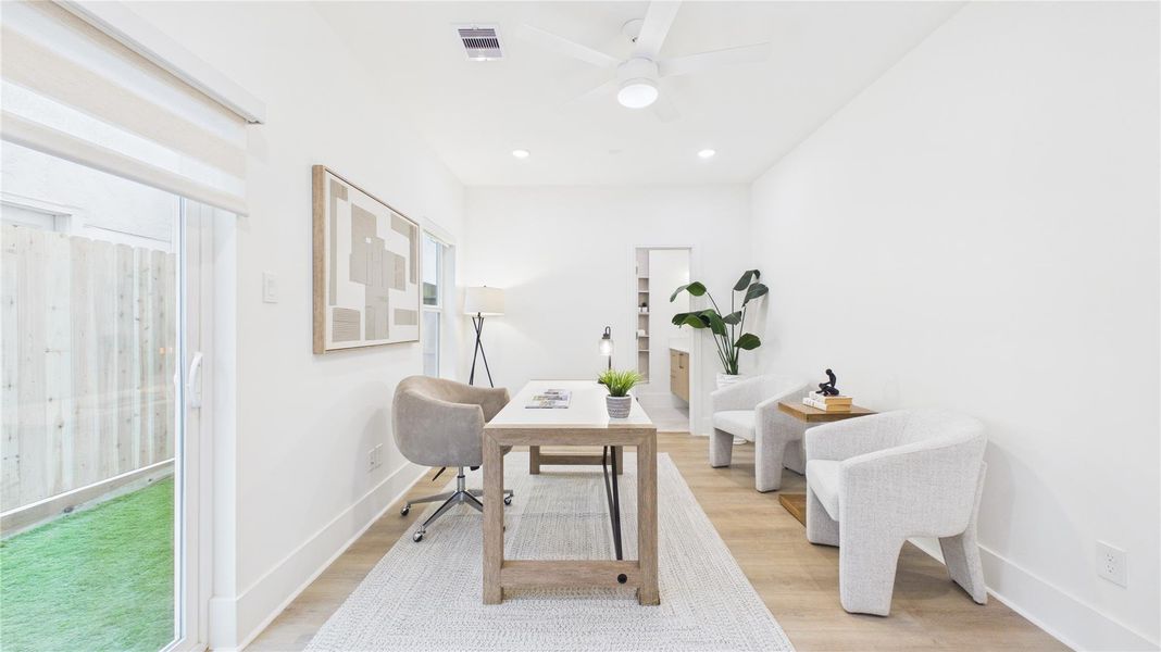 Bright and modern home office with a minimalistic design. The room features a large window for natural light, white walls, and light wood flooring. It includes a central desk, comfortable seating, and decorative plants, creating an inviting workspace.
