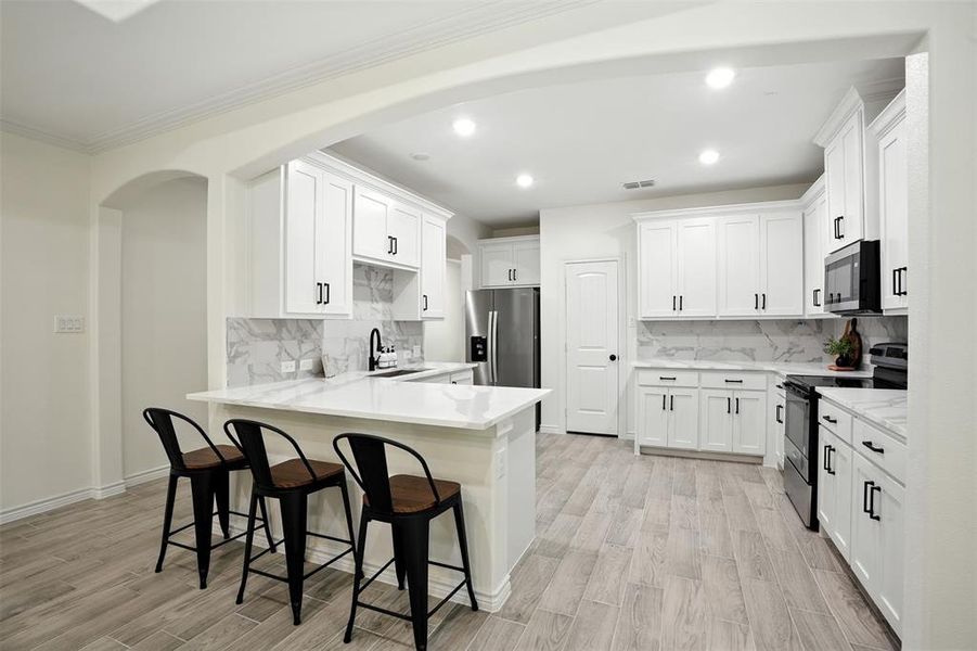 Kitchen featuring appliances with stainless steel finishes, a kitchen bar, white cabinets, recessed lighting, and a peninsula
