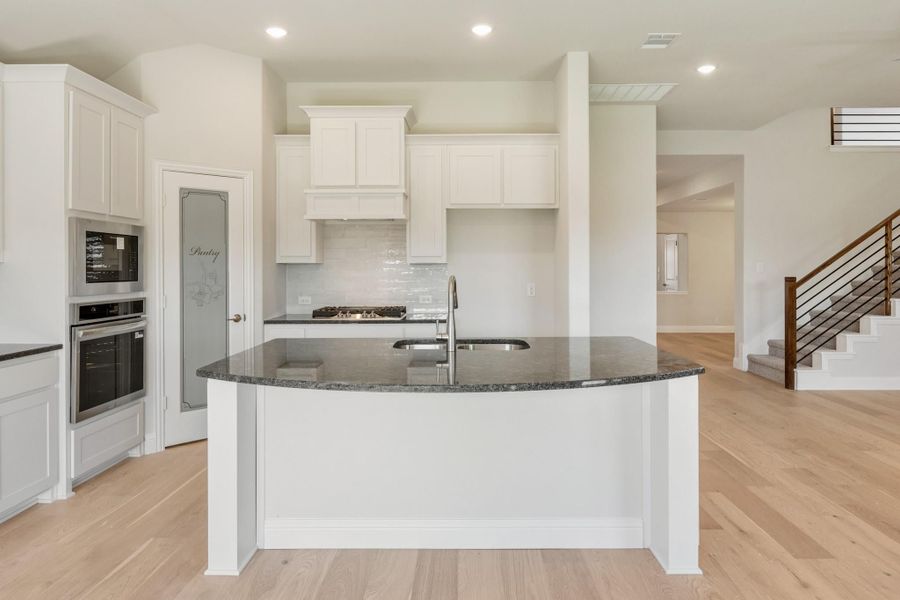 Kitchen with curved island, dark granite countertop, white cabinets, and stainless steel appliances on light hardwood floors Kitchen with curved island, dark granite countertop, white cabinets, and stainless steel appliances on light hardwood floors