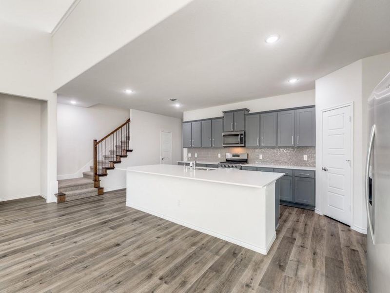 Kitchen featuring gray cabinets, a kitchen island with sink, tasteful backsplash, light wood finished floors, and recessed lighting