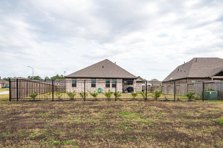 This photo shows a suburban backyard with a black metal fence, a grassy area, and a view of a brick house with a gray roof. The yard is spacious and enclosed, offering privacy and space for outdoor activities. This photo shows a suburban backyard with a black metal fence, a grassy area, and a view of a brick house with a gray roof. The yard is spacious and enclosed, offering privacy and space for outdoor activities.
