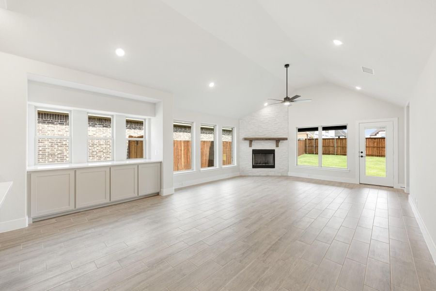 Open living room with vaulted ceiling, brick fireplace, ceiling fan, and light wood-look tile floors