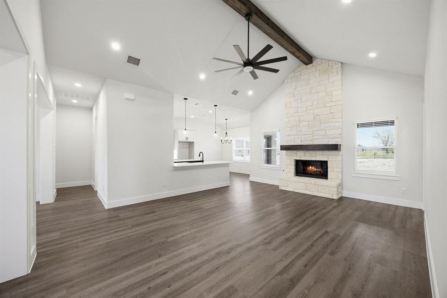 Spacious living area featuring a vaulted ceiling with exposed wood beam, a stone-clad fireplace with a dark wood mantle, and wood-finish flooring