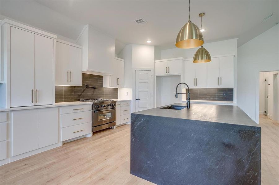 Kitchen with light hardwood / wood-style floors, tasteful backsplash, stainless steel stove, hanging light fixtures, and white cabinets