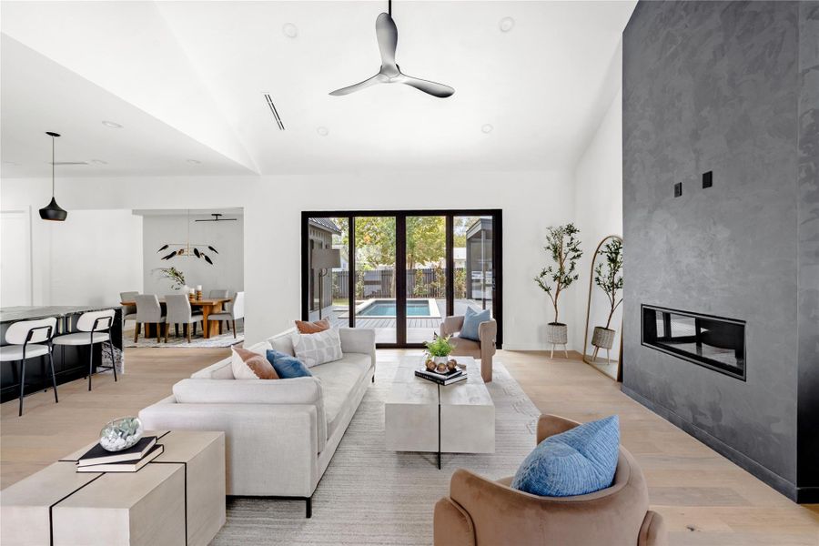Living area featuring light wood-style flooring, lofted ceiling, a large fireplace, and ceiling fan