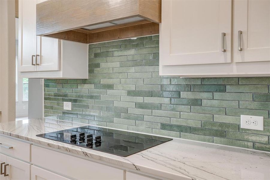 Kitchen featuring white cabinets, decorative backsplash, light stone counters, and black electric cooktop