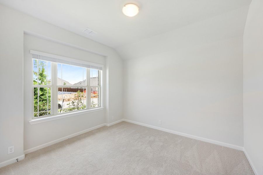Empty bedroom with vaulted ceiling, carpet flooring, and large window with outdoor view