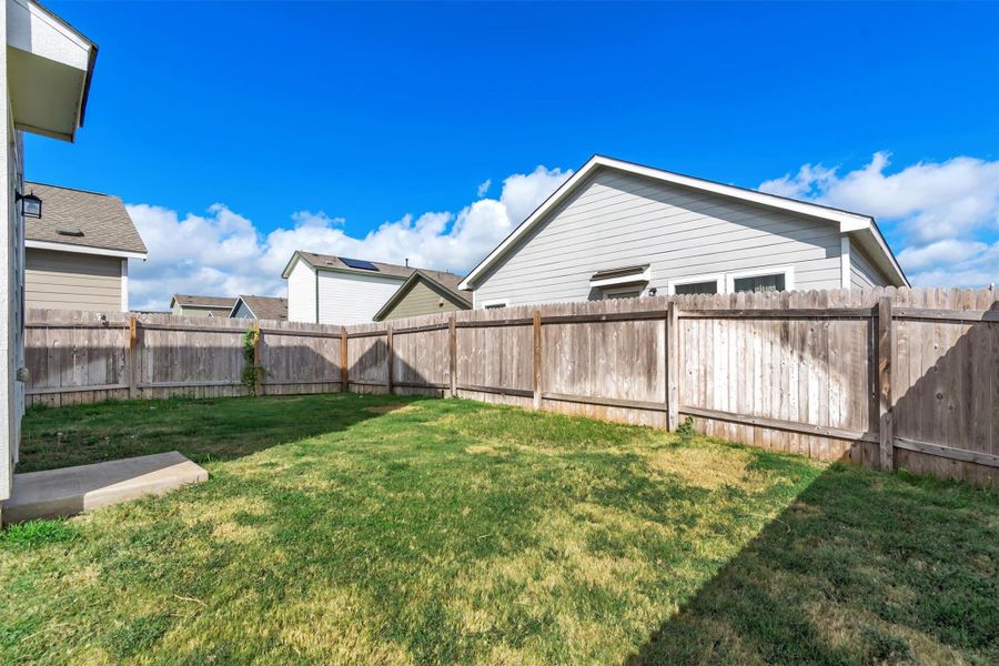 A fully fenced backyard provides a grassy lawn area under open blue skies. A fully fenced backyard provides a grassy lawn area under open blue skies.