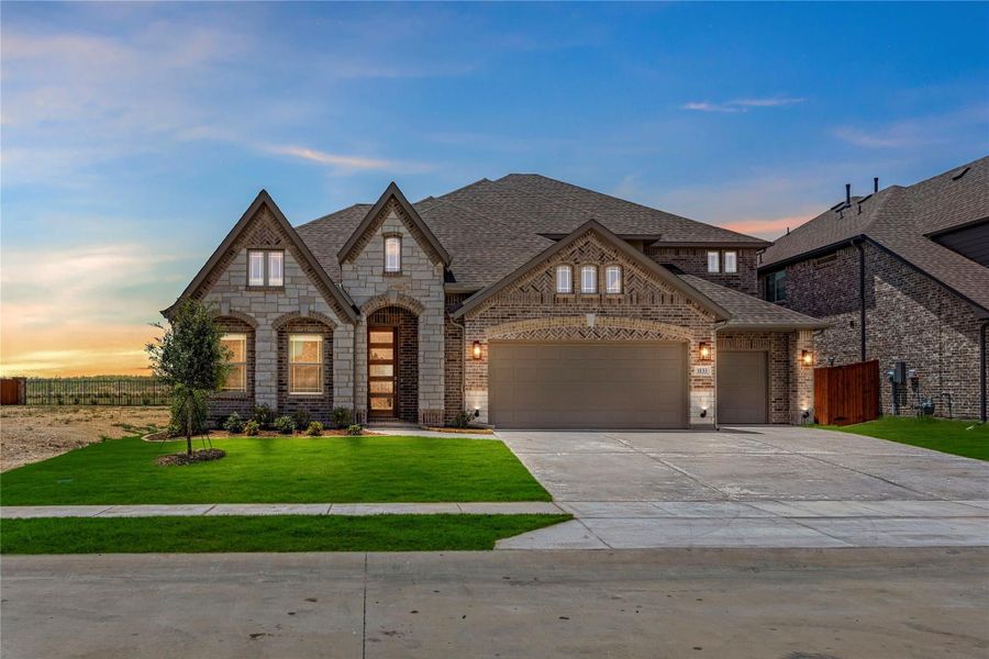 Single-story brick and stone home with two-car garage, arched entry, and green front lawn at dusk
