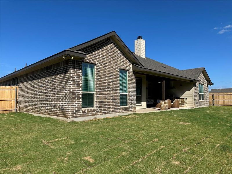 Spacious outdoor living area with a covered patio, brick and stone veneer exterior, and a large grassy yard