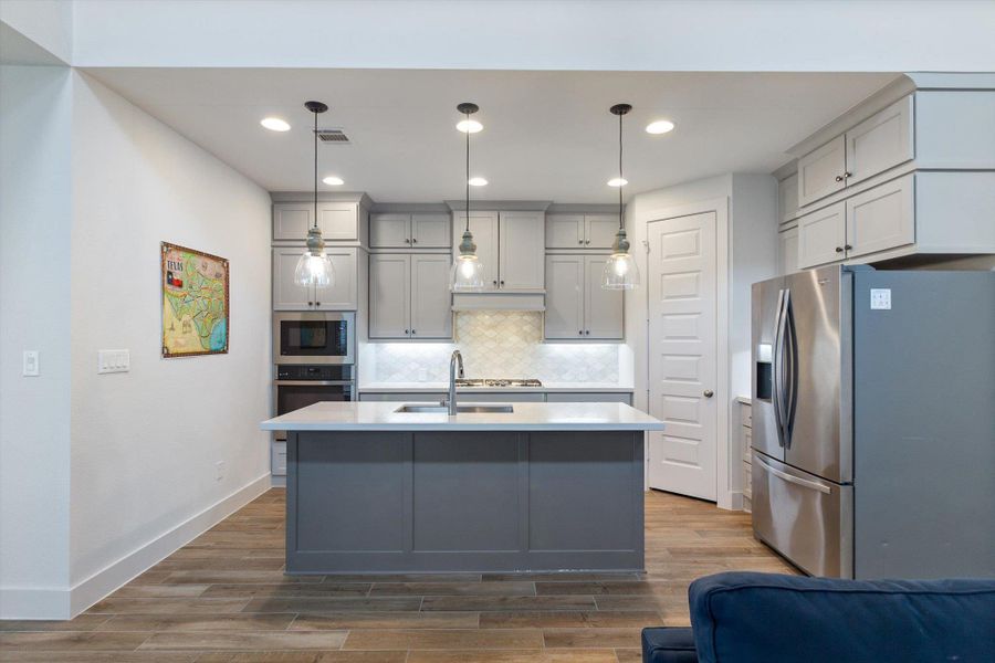 Kitchen featuring gray cabinetry, appliances with stainless steel finishes, decorative backsplash, decorative light fixtures, and light wood finished floors