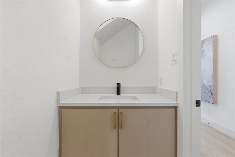 Contemporary vanity with light-colored cabinetry and brass hardware, featuring a white countertop with integrated sink and matte black faucet Contemporary vanity with light-colored cabinetry and brass hardware, featuring a white countertop with integrated sink and matte black faucet