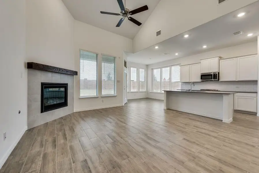 Kitchen featuring high vaulted ceiling, light wood-type flooring, a tiled fireplace, and white cabinets