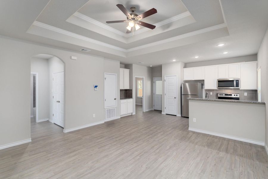 Open-concept living space featuring wood-finish flooring, a tiered tray ceiling with a ceiling fan, and recessed lighting