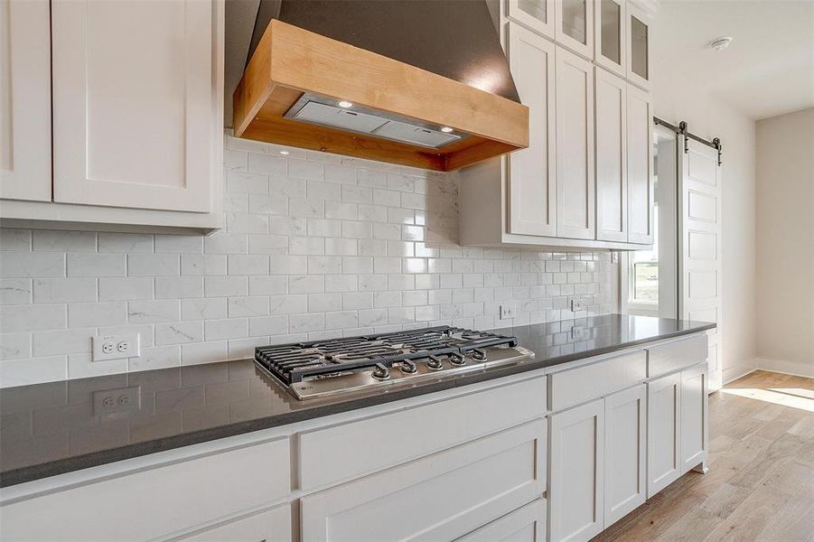 Kitchen with white cabinetry, light hardwood / wood-style flooring, a barn door, wall chimney exhaust hood, and decorative backsplash