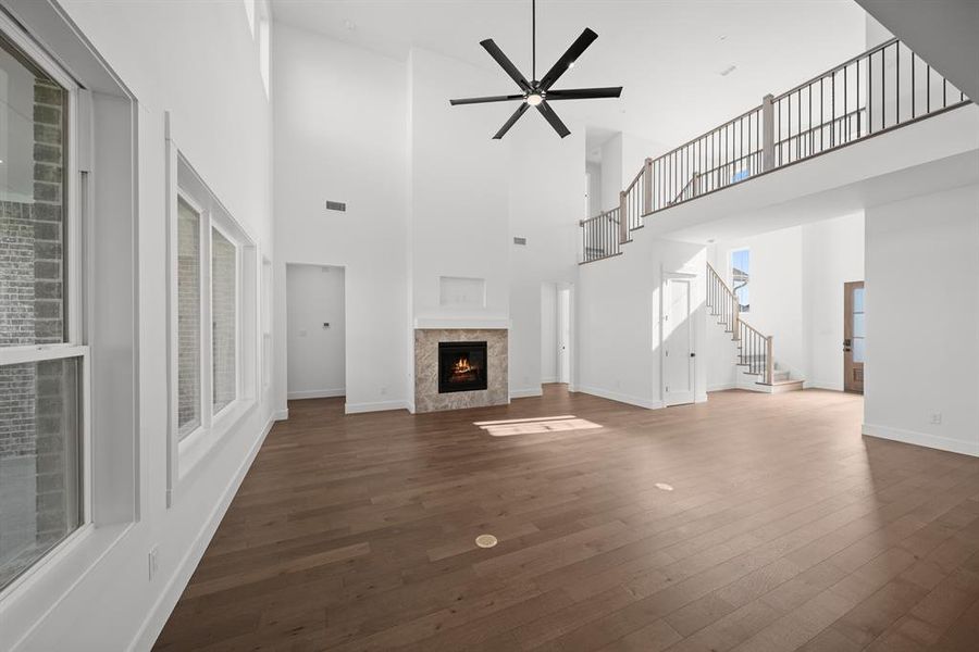 Unfurnished living room with a tiled fireplace, stairs, a ceiling fan, dark wood-type flooring, and a towering ceiling