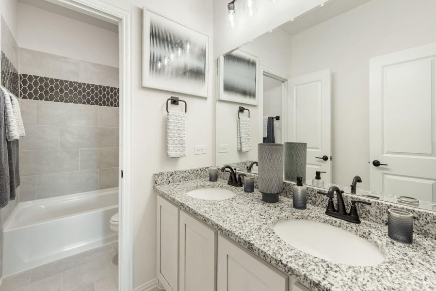 Bathroom with double granite sink vanity, large mirror, and tiled shower-tub combo with hexagon accent strip