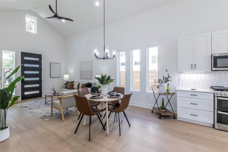 Dining area featuring high vaulted ceiling, light wood finished floors, ceiling fan, a chandelier, and recessed lighting