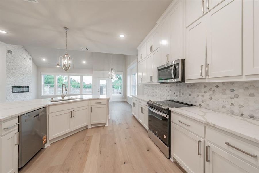 Kitchen featuring appliances with stainless steel finishes, light wood-style floors, white cabinets, decorative light fixtures, and healthy amount of natural light