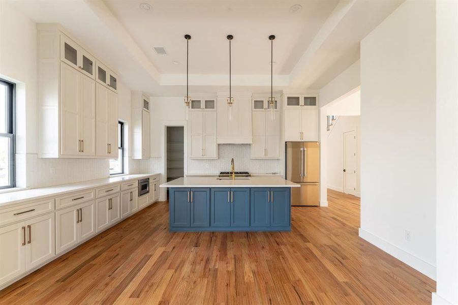 Kitchen with a raised ceiling, hanging light fixtures, stainless steel appliances, blue cabinets, and white cabinetry