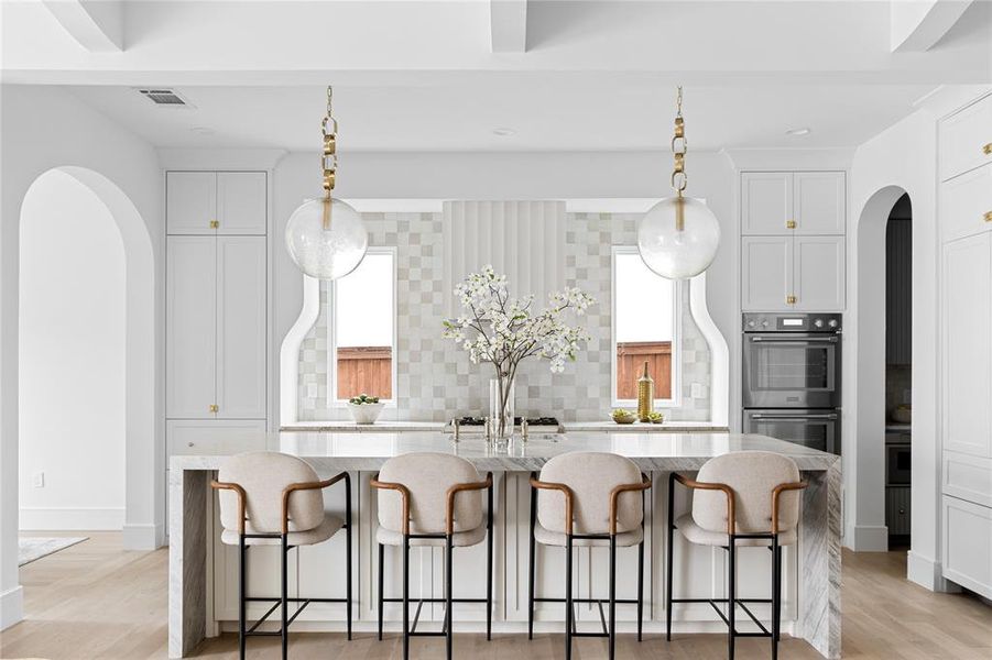 Kitchen with arched walkways, light stone counters, a breakfast bar, a center island with sink, and recessed lighting