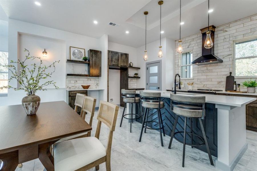 Kitchen with wall chimney exhaust hood, pendant lighting, decorative backsplash, a kitchen breakfast bar, and sink